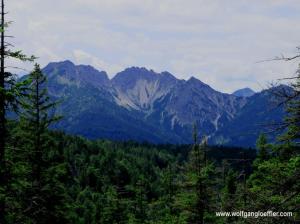 PAnoramablick ueber einen bewaldeten Berghang auf felsige Gipfel