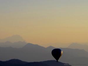 Ein Heißluftballon schwebt im Sonnenuntergang vor beeindruckender Alpenkulisse