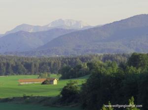 Luftaufnahmeeiner Scheune auf einer Wiese mit Berggipfeln im HIntergrund